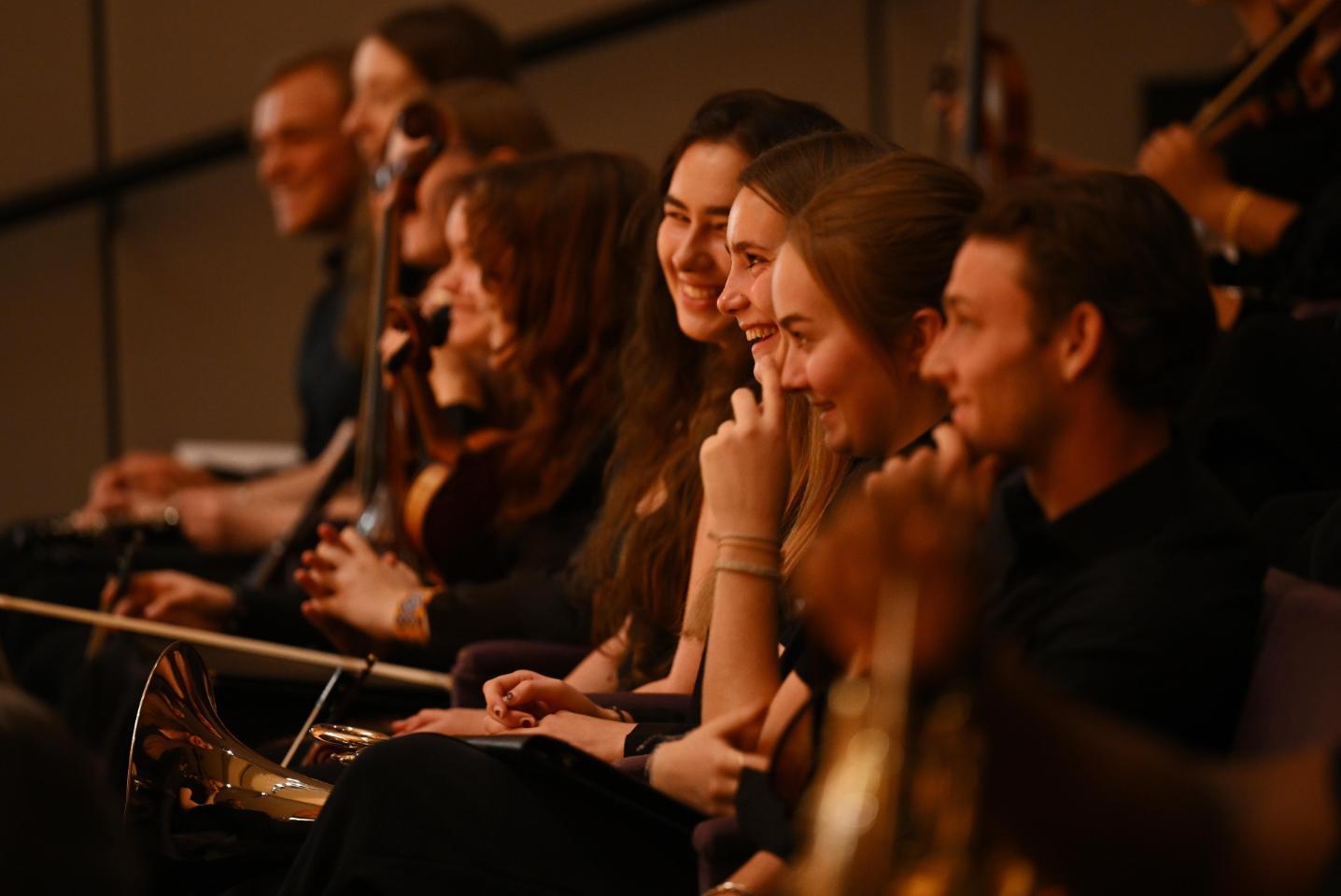 A photo of students in the Connecticut College Orchestra laughing during rehearsal.