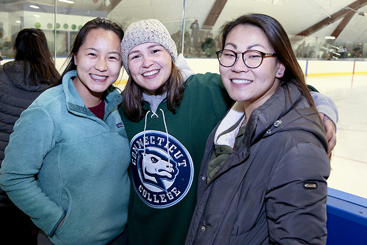 Three students, including one wearing a green Conn hockey jersey, pose together before the start of the Green Dot Hockey Game.