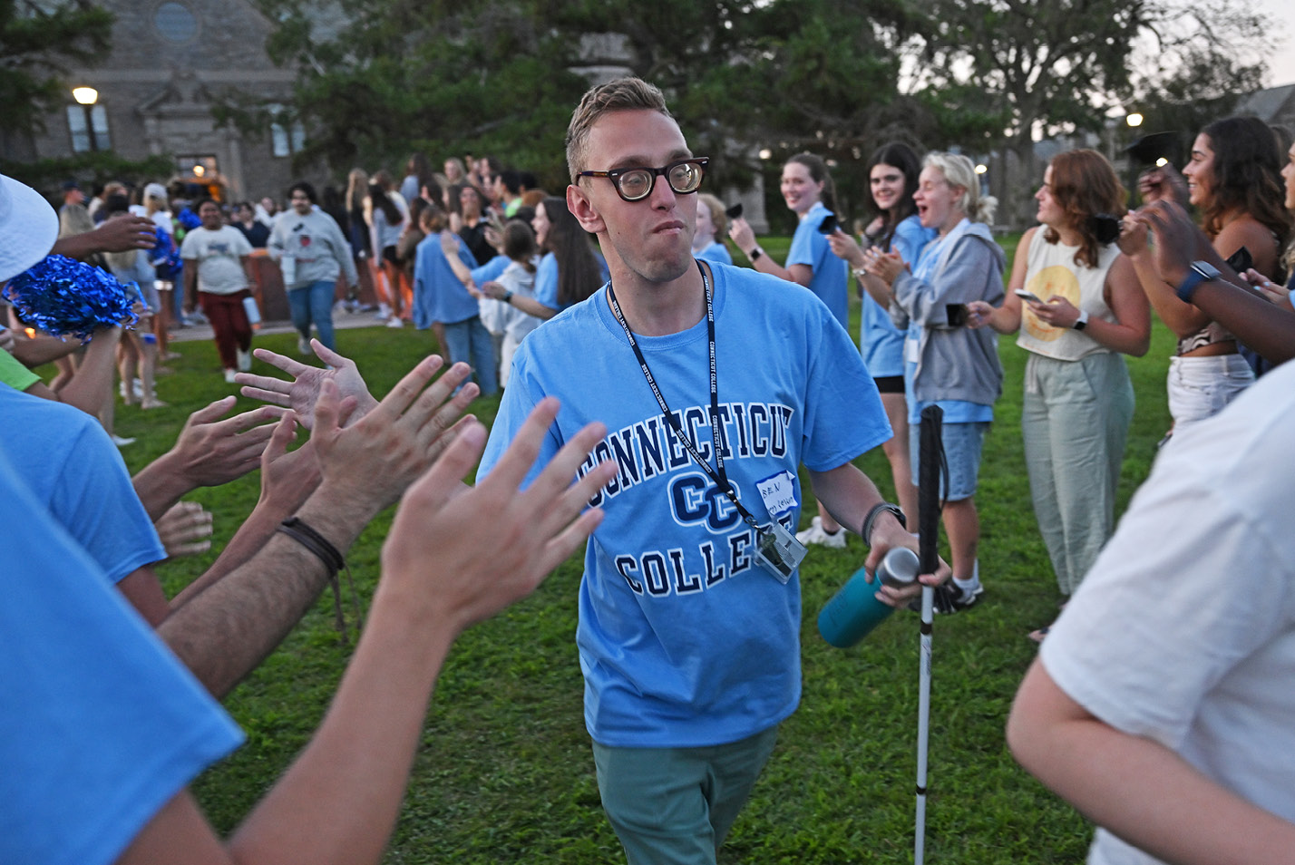 A student with a cane walks high-fives other students in a line.