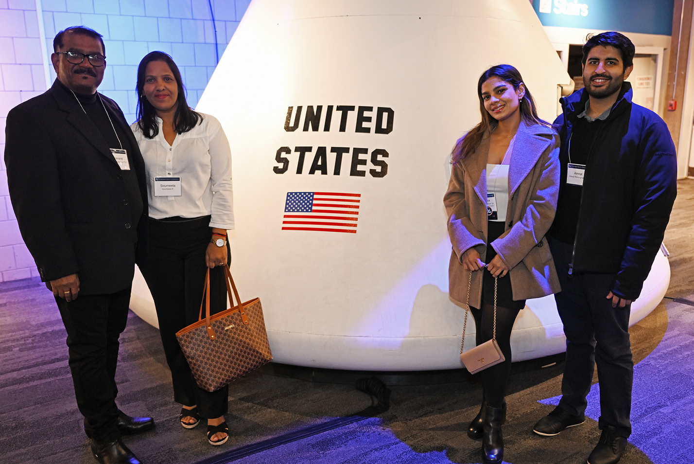 Alums pose in front of a NASA space capsule at the alumni holiday party at the Boston Museum of Science.