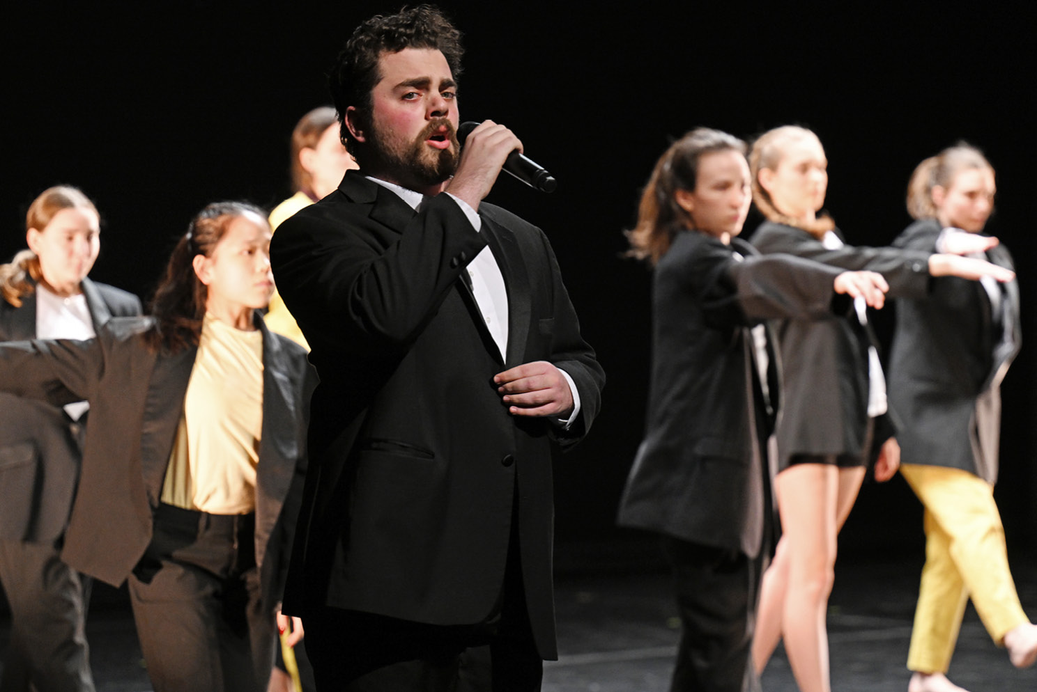 Student singing with dancers in the background