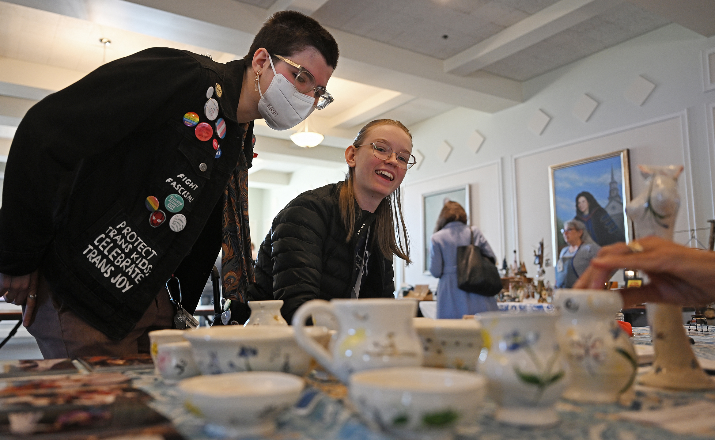 Two students lean over to look at items for sale at a craft fair.