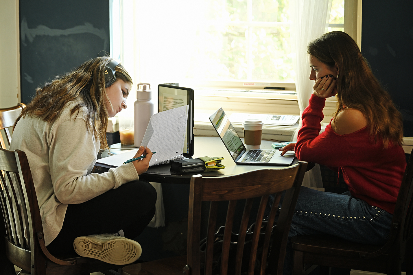 Two students work on their laptop computers in a coffee shop.