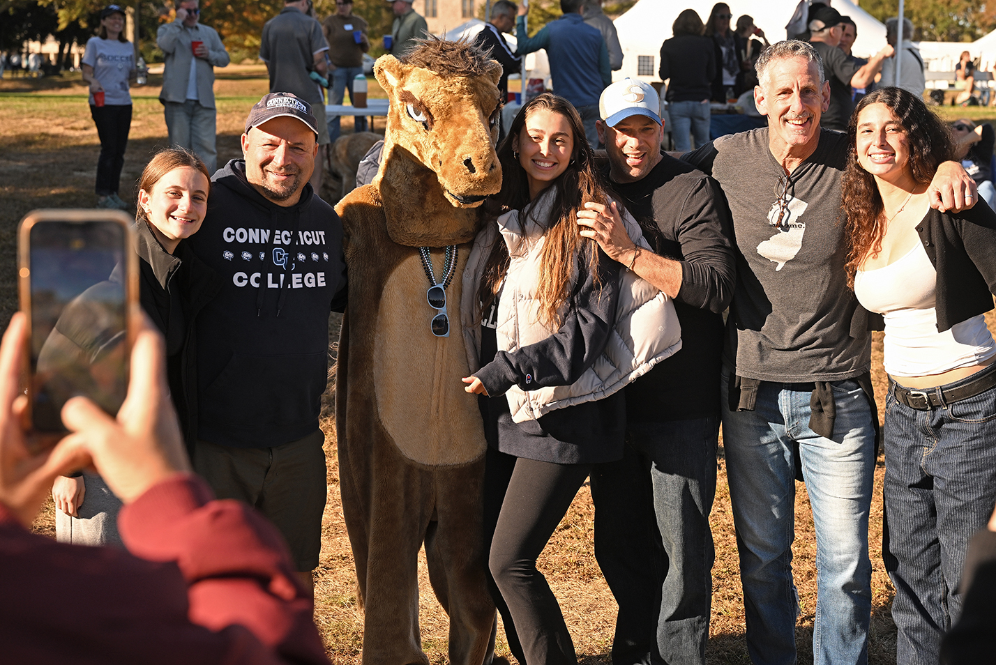 A group of college sports fans pose with a camel mascot.