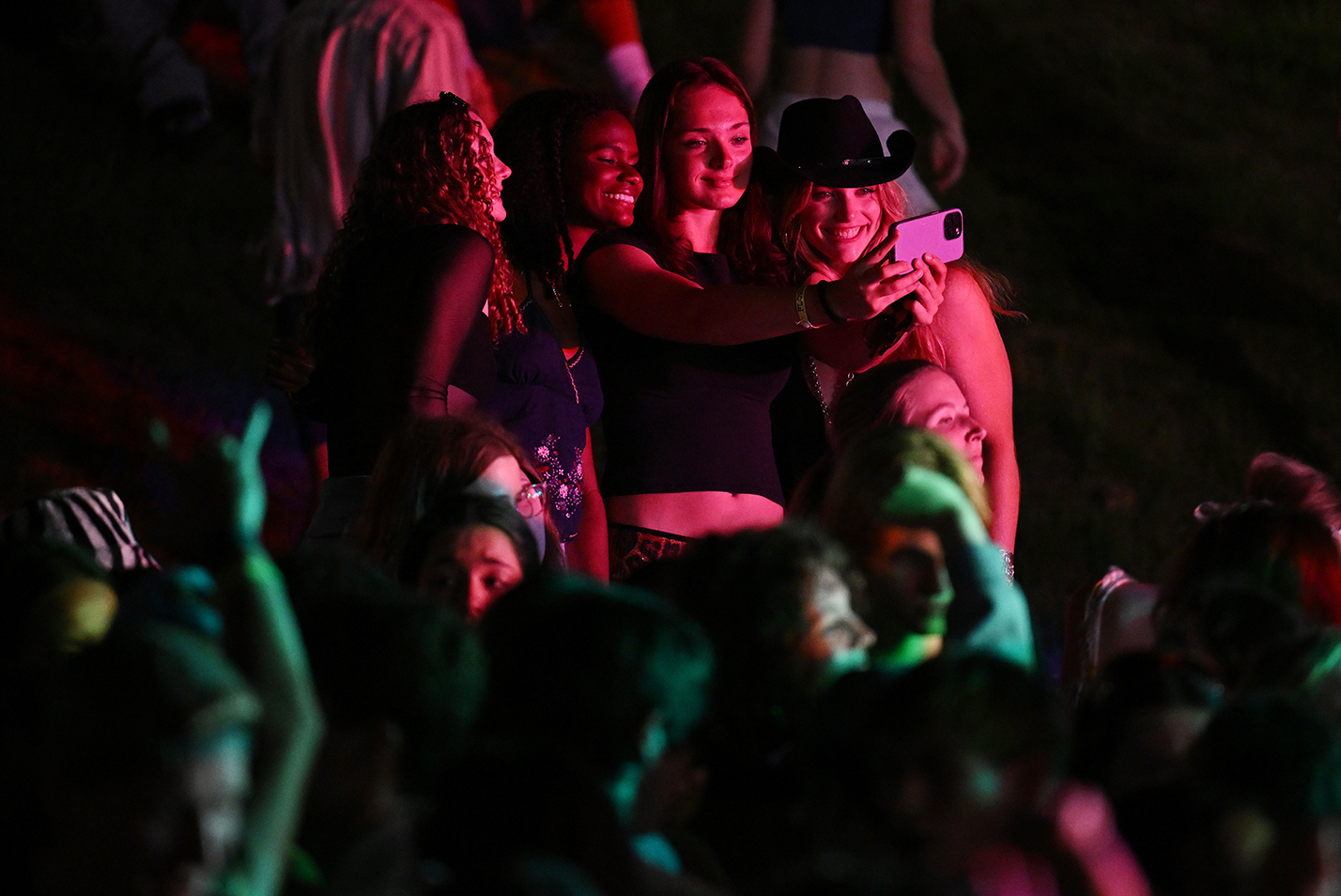 Students take a photo together in the glow of the stage lights during a spring music festival.